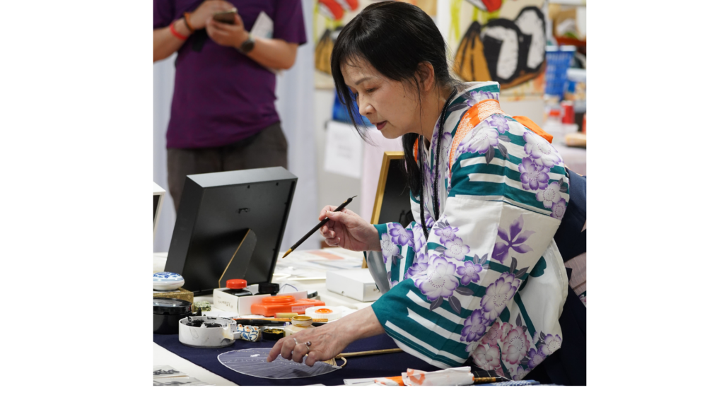 La maître calligraphe Kimiko Nakatani décore un éventail japonais uchiwa au festival Nishiki Japan 2025.